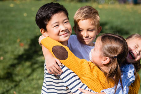 Asian boy looking at camera while hugging smiling friends outdoors