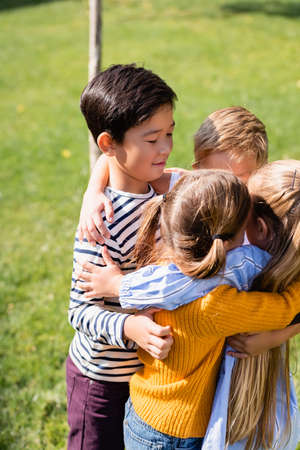 Asian boy hugging friends on blurred foreground in parkの写真素材
