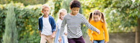 Asian boy running near friends on blurred background in park, banner