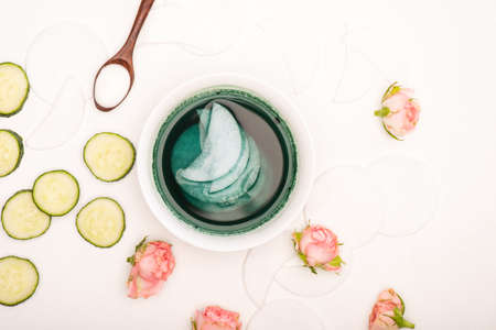 top view of bowl with tonic and cotton pads, tea roses, fresh cucumber slices and spoon with cosmetic cream on whiteの写真素材