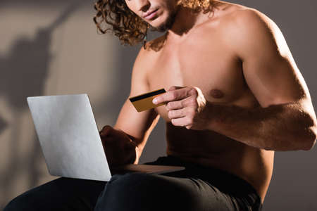 cropped view of sexy shirtless man holding laptop and credit cardの写真素材