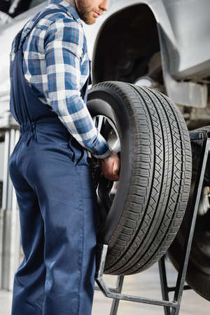 cropped view of mechanic holding wheel near lifted car on blurred backgroundの写真素材
