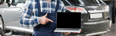 partial view of mechanic pointing at laptop with blank screen near car on blurred background, bannerの写真素材