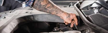 cropped view of tattooed technician checking engine oil in car, bannerの写真素材