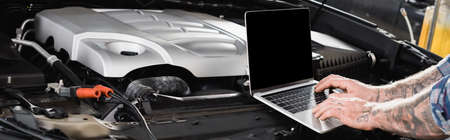 cropped view of tattooed mechanic making car diagnostic on laptop near engine compartment, banner