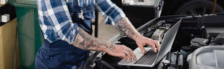 partial view of workman making diagnostic of car engine compartment with laptop, banner