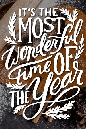 Top view of christmas cookies with cutter shapes, pine cones and cinnamon sticks near its the most wonderful time of the year letteringの写真素材