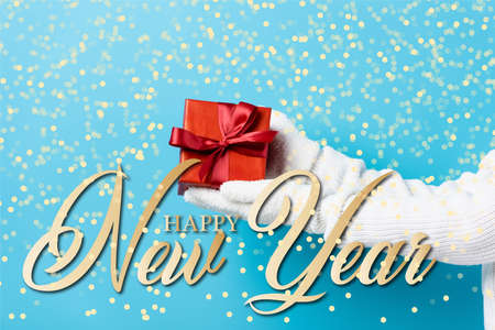cropped view of young woman in gloves holding gift box near happy new year lettering on blue
