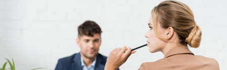 Thoughtful female executive with pen, looking away with blurred colleague on background, bannerの写真素材