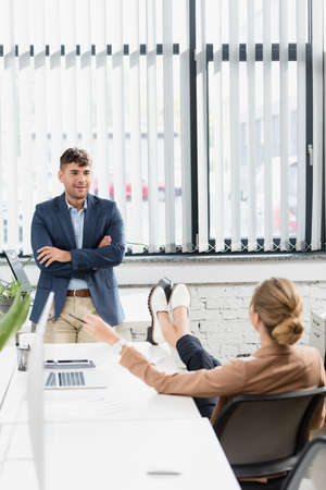 Back view of businesswoman with crossed legs sitting at office chair near colleague during break in office on blurred foregroundの写真素材