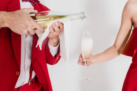 Cropped view of man in red suit pouring champagne in glass near woman on gray backgroundの写真素材
