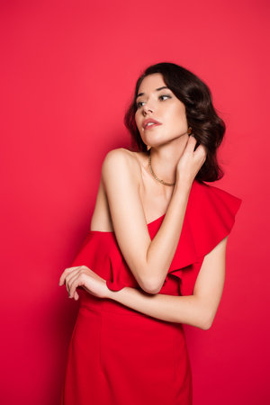 Brunette woman in red dress looking away on red backgroundの写真素材