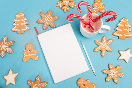 top view of gingerbread cookies, candy canes and blank notebook on blue backgroundの写真素材