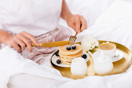 Cropped view of cutlery in hands of woman near pancakes with berries, coffee and carnation on...
