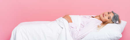 Young woman in pajamas lying on pillow with blanket on pink background, bannerの写真素材