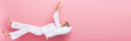 Young woman in pajamas and blindfold lying on pillow on pink background, banner