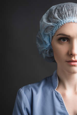 partial view of nurse in medical cap looking at camera isolated on dark gray