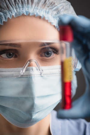 close up of nurse in medical cap, mask and goggles holding test tube on blurred foregroundの写真素材