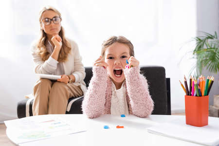 little girl patient screaming and clenching figures while visiting psychologist