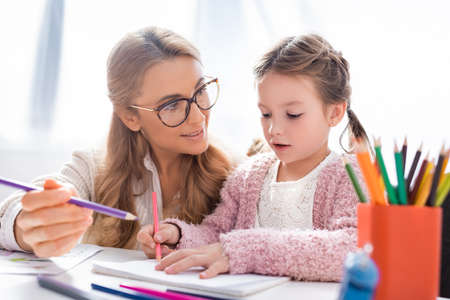 little girl drawing pictures with colorful pencils while visiting psychologist