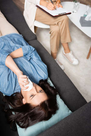 brunette woman wiping nose with tissue while therapist making notesの写真素材