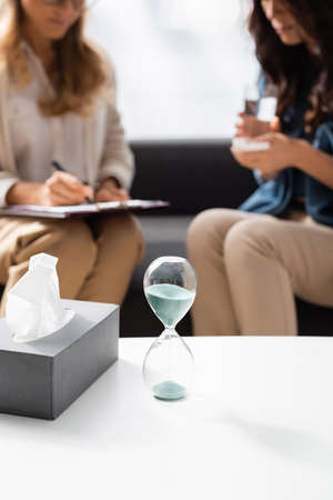 blurred view of doctor and patient and hourglass, tissues on foreground