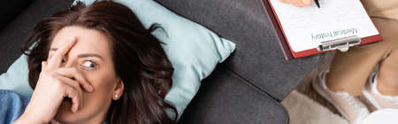 terrified brunette woman covering face while therapist writing in medical history, bannerの写真素材