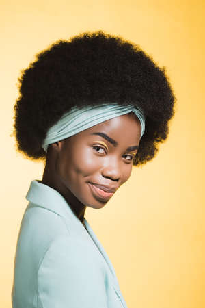 smiling african american young woman in blue stylish outfit isolated on yellow