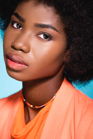 african american young woman in orange stylish outfit isolated on blue