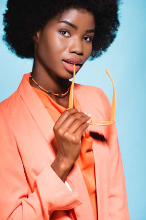 african american young woman in orange stylish outfit isolated on blue background