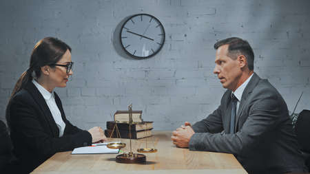 Insurance agents looking at each other near notebook, scales and books on table