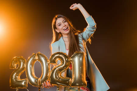 cheerful woman smiling and holding 2021 numbers balloons on blackの写真素材
