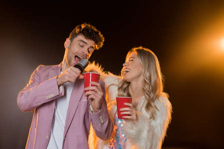 man singing while holding microphone near woman with plastic cup on blackの写真素材