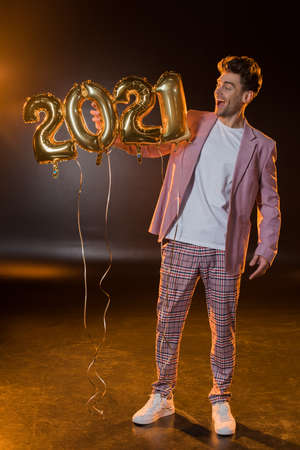 full length of cheerful man holding 2021 numbers balloons on blackの写真素材