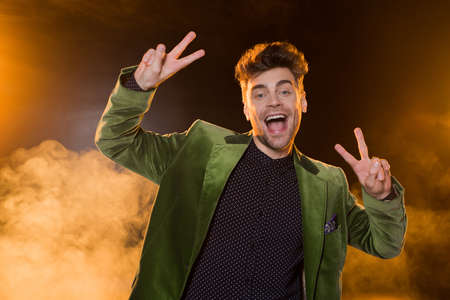 excited man in green blazer showing peace sign on black with smoke
