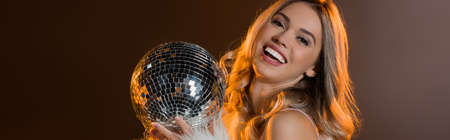 pleased blonde woman holding disco ball on black, bannerの写真素材