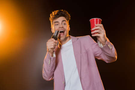 man singing while holding microphone and plastic cup on blackの写真素材