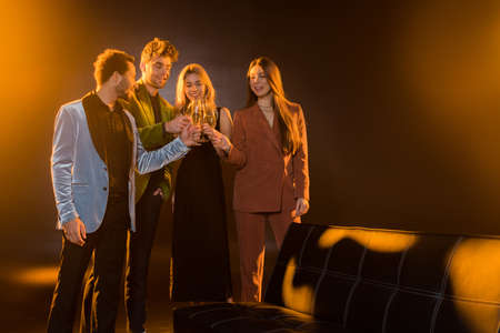 multicultural friends clinking glasses of champagne near sofa on blackの写真素材