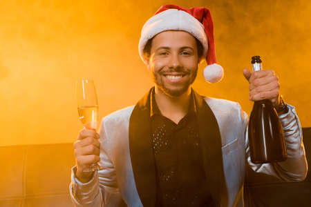 happy african american man holding bottle of champagne and glass on orange with smoke