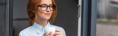 Positive businesswoman with coffee cup looking away at window, bannerの写真素材