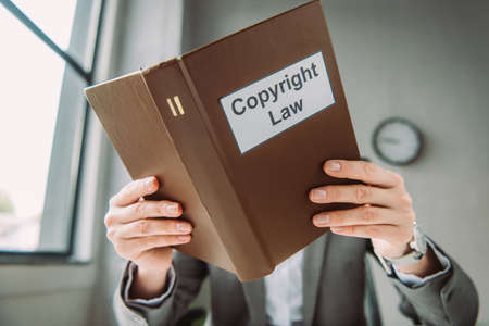 Book with copyright law lettering covering face of female lawyer on blurred background