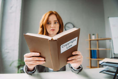 Low angle view of book with copyright law lettering in hands of female lawyer sitting at workplace on blurred backgroundの写真素材