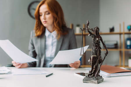 Themis figurine on table with blurred lawyer with paper sheets on backgroundの写真素材