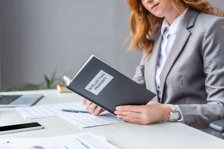 Cropped view of female lawyer holding book with intellectual property lettering at workplace on blurred backgroundの写真素材