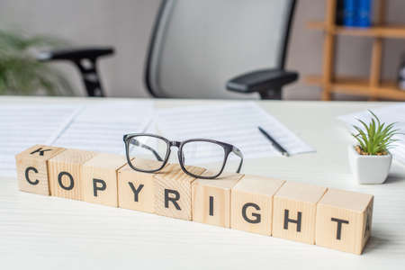 Close up of eyeglasses on wooden cubes with copyright lettering with blurred workplace on backgroundの写真素材