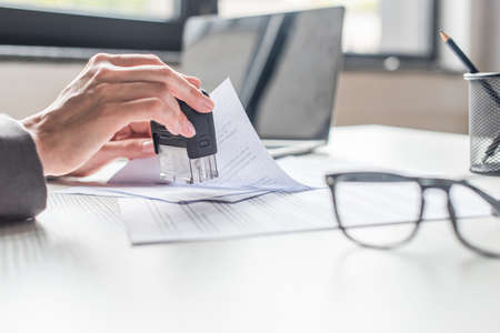 Cropped view of businesswoman putting stamp in document at workplace on blurred backgroundの写真素材