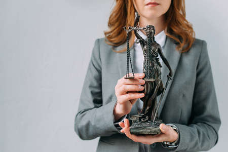 Cropped view of female lawyer holding themis figurine on grayの写真素材