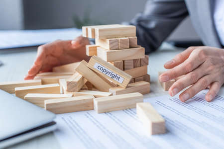 Cropped view of lawyer holding hands near blocks wood game construction with copyright lettering...