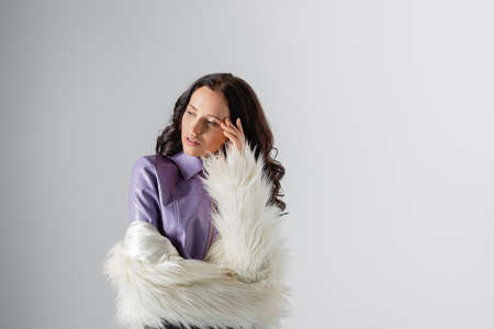 brunette young woman in stylish white faux fur jacket posing on gray backgroundの写真素材