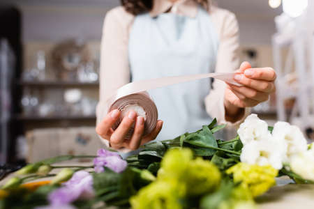cropped view of florist holding decorative ribbon near eustoma flowers while making bouquet on blurred foregroundの写真素材